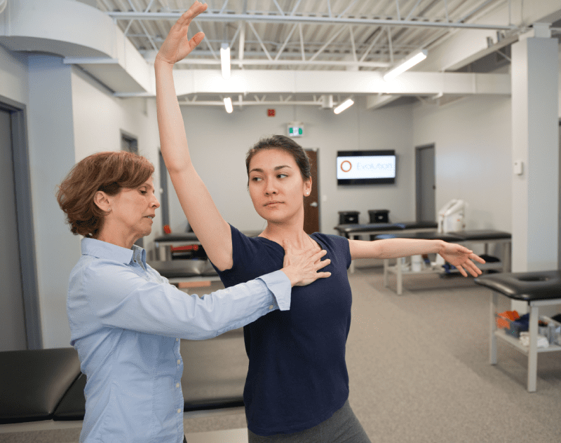 The woman being taught is holding her arms up, possibly learning a dance move or practicing her posture