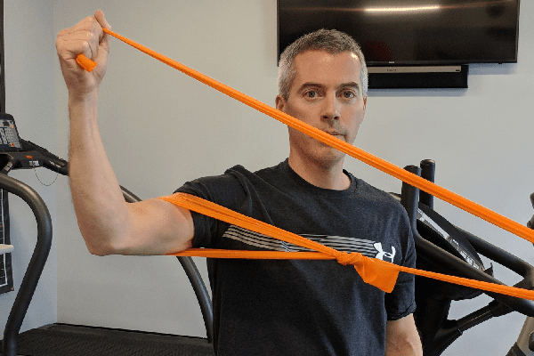 a man standing in a gym, holding a yellow resistance band in his hand