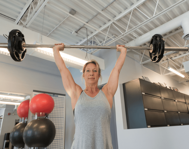 a woman in a gym, lifting a barbell above her head as she performs a weightlifting exercise