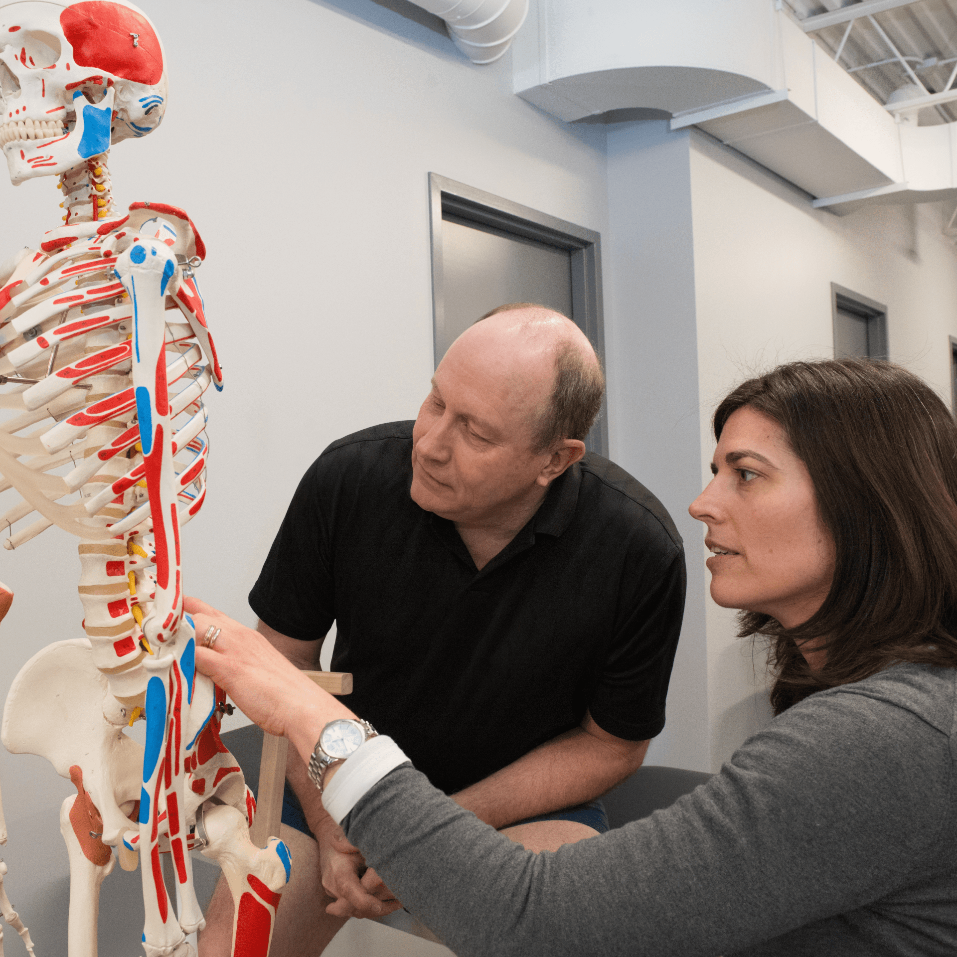 a man and a woman standing next to each other, both looking at a skeleton